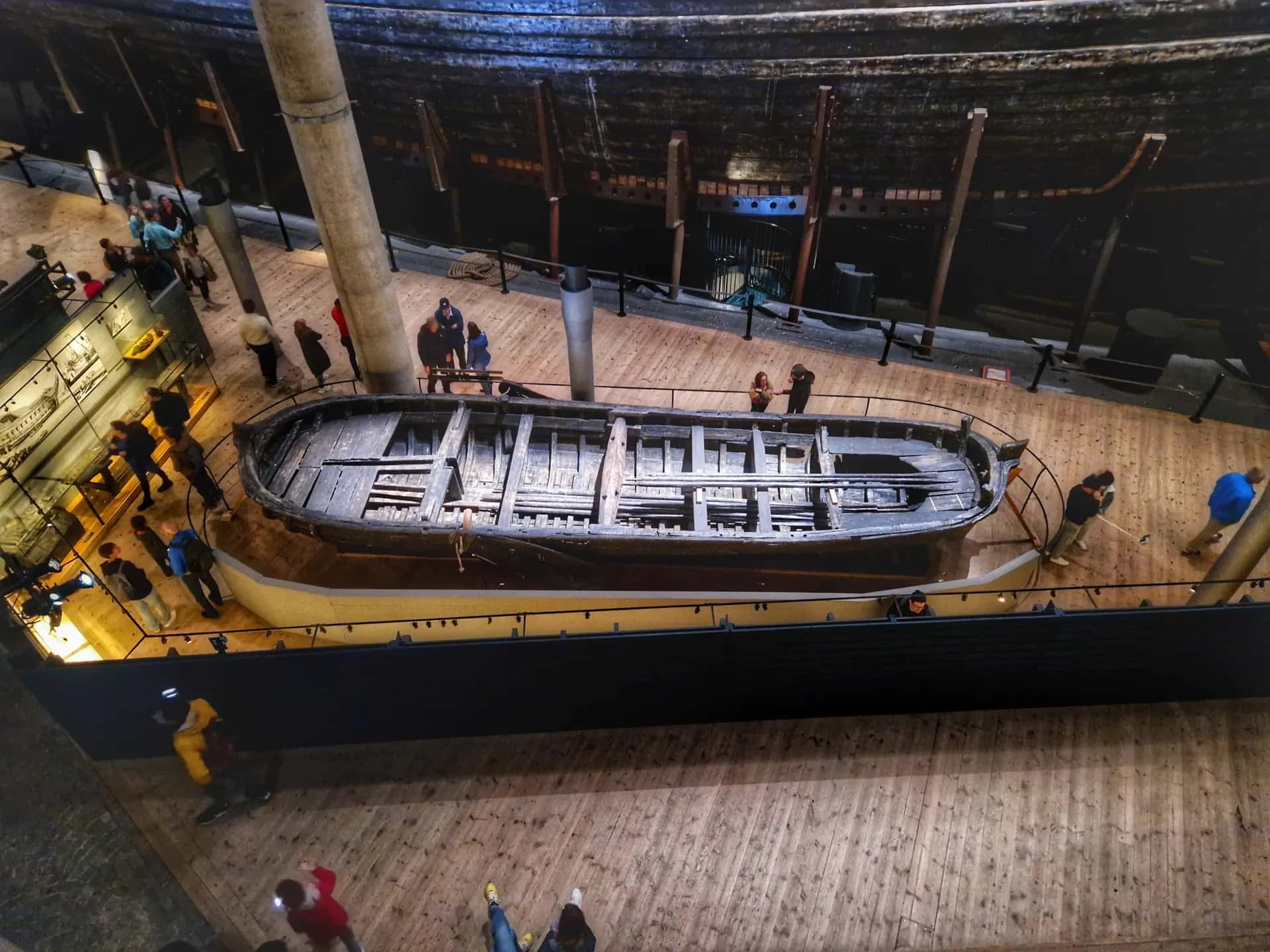Inifrån ett museum med ett stort, mörkt skepp och en mindre träbåt. Besökare på trägolvet
