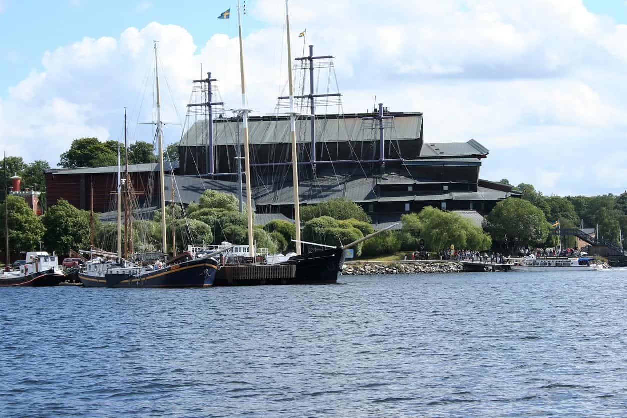 Stora segelfartyg vid kaj framför Vasamuseet och en folksamling vid vattnet, under delvis molnig himmel