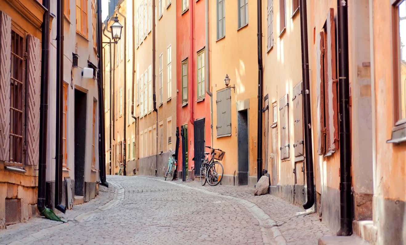 Smal kullerstensgata kantad av gamla färgglada hus med fönsterluckor. Två cyklar står parkerade
